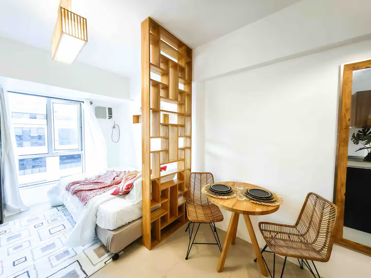 Casa Siempre: a bed beside a window, a timber room divider, rattan seating and a patterned rug.