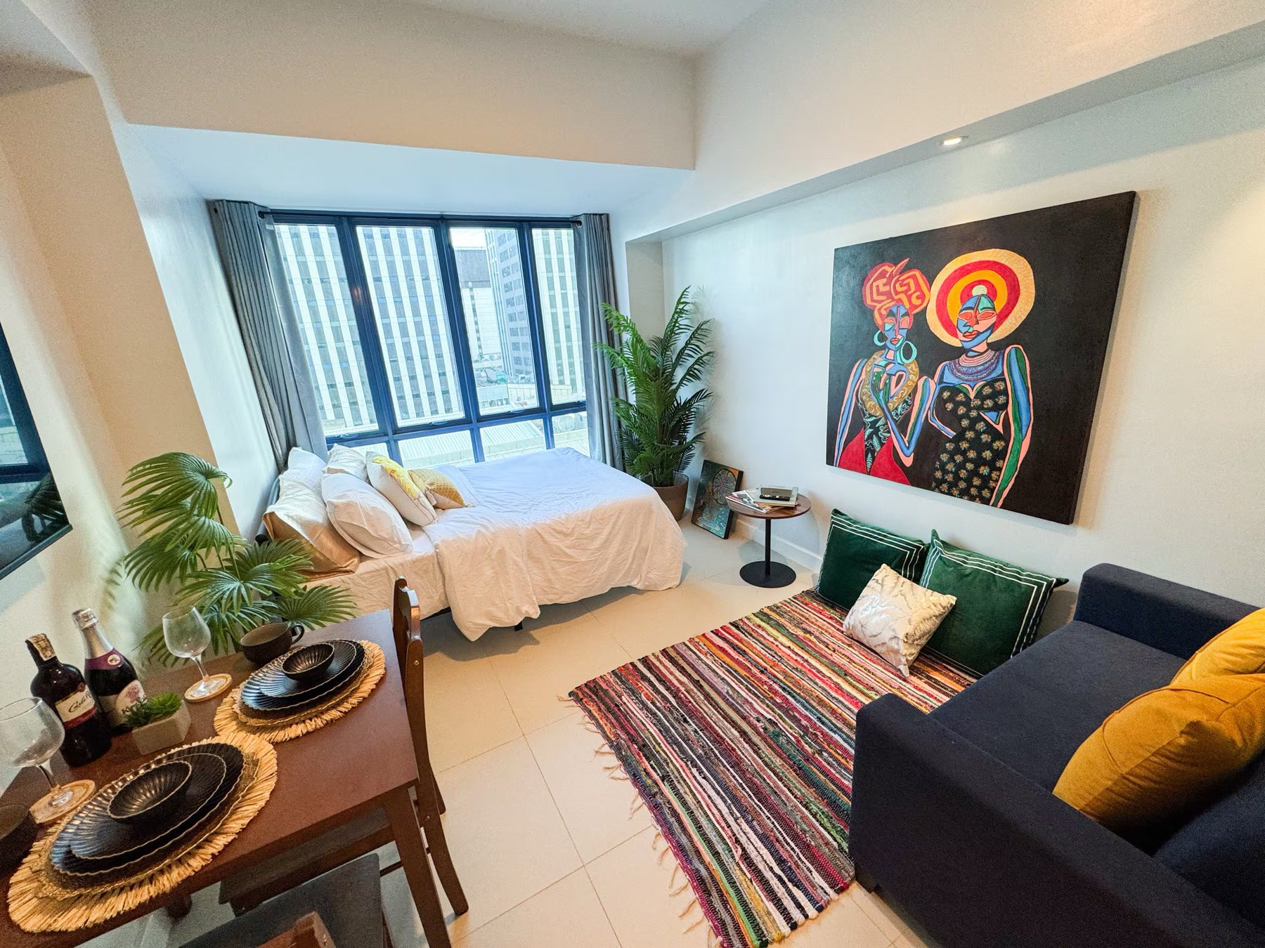 Estudio La Vida at 38 Park Avenue: a bed beside floor-to-ceiling windows, a navy sofa, a large figurative painting and a woven rug.