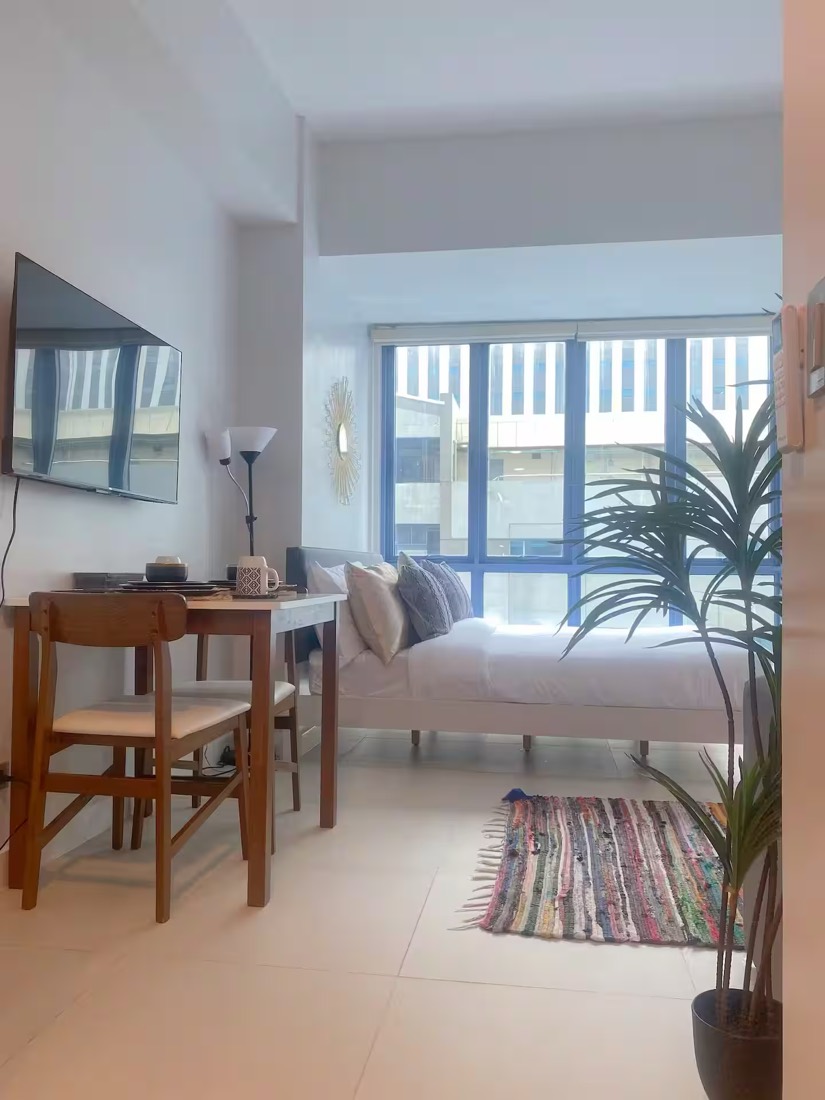 A made bed beside a workspace and full-height window in a Siempre Stays studio, reset for the next guest.