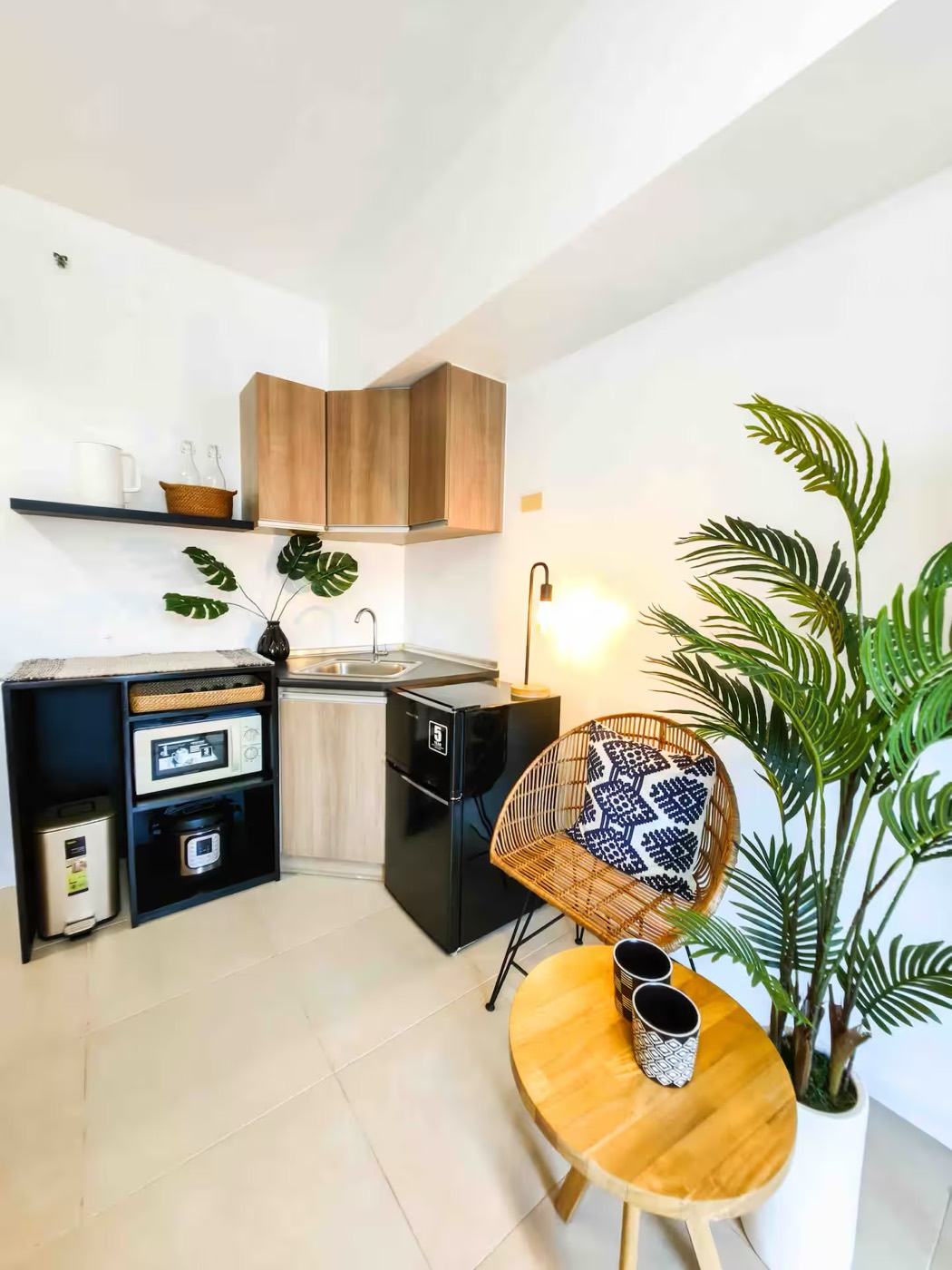 A compact kitchenette in a Siempre Stays studio, with plants, dark ceramics and a rattan chair.